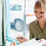 Zwei Frauen unterhalten sich an einem Tisch. Eine hält ein Klemmbrett und einen Stift in der Hand und lächelt, während sie am Fenster sitzt.