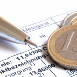 Kugelschreiber und Euromünzen auf einer Stromrechnung mit der Aufschrift „Strom“.