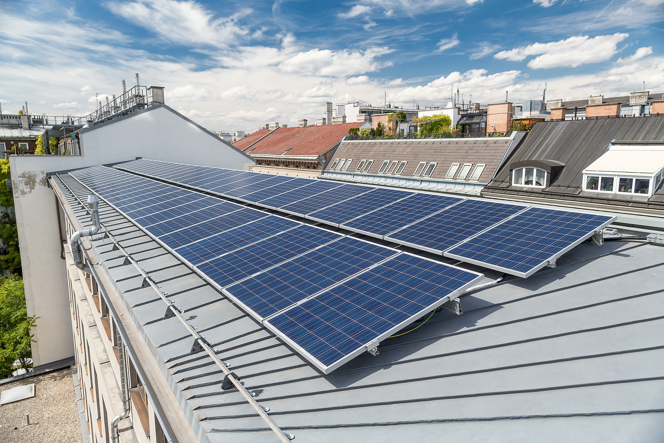 Sonnenkollektoren auf dem Metalldach der Berufsschule Apollogasse unter blauem Himmel mit Wolken.  überblicken Stadtgebäude.
