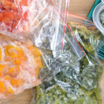 Beutel mit gefrorenem Gemüse und ein Behälter mit gefrorenen Spinatwürfeln auf einer Holzoberfläche.