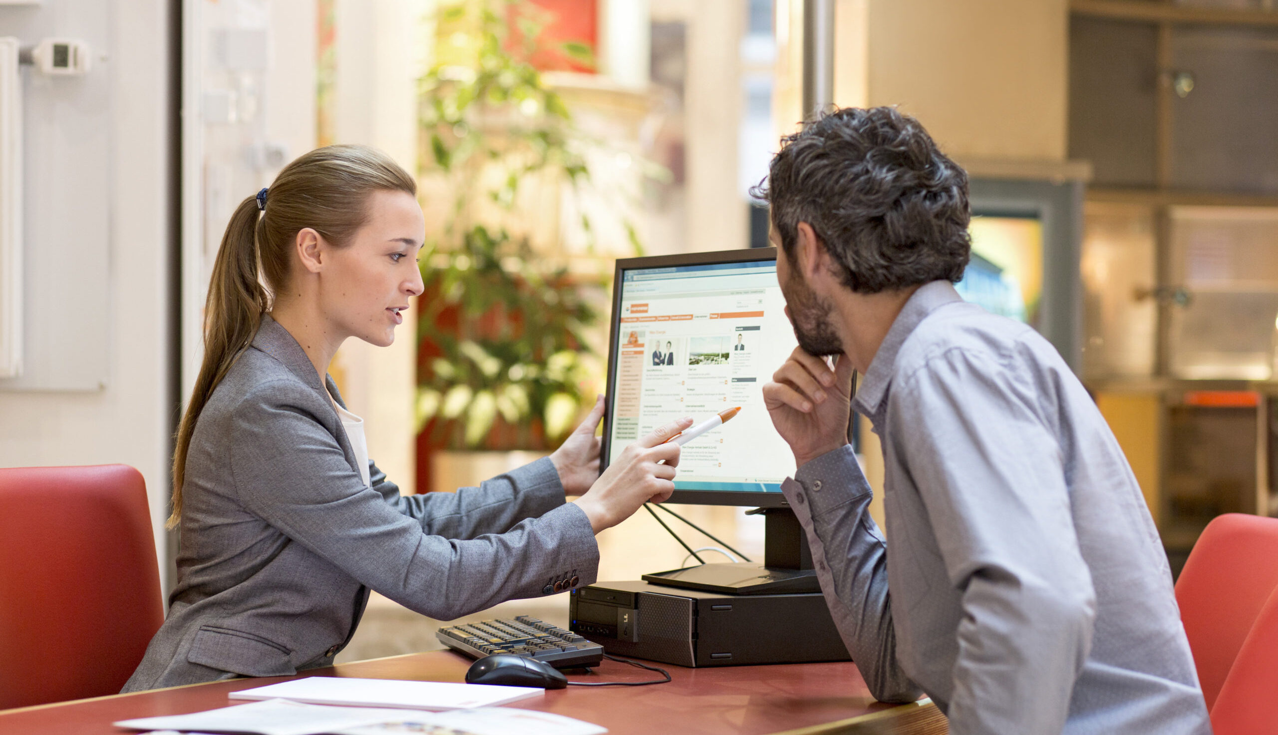 Eine Frau erklärt einem Mann etwas und zeigt ihm etwas auf dem Bildschirm
