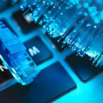 Blaues Ethernet-Kabel und Glasfaserkabel auf einer Tastatur, als Symbol für Hochgeschwindigkeits-Internet und Technologie.