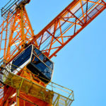 Orangefarbener Baukran vor einem klaren blauen Himmel.