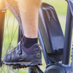 Person, die an einem sonnigen Tag ein schwarzes E-Bike fährt, Nahaufnahme der Pedale und des Hinterrads.