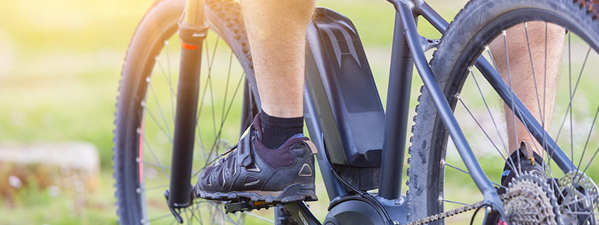 Person, die an einem sonnigen Tag ein schwarzes E-Bike fährt, Nahaufnahme der Pedale und des Hinterrads.