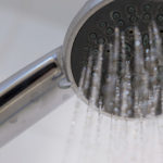 Nahaufnahme eines Duschkopfs mit sprühendem Wasser in einem Badezimmer.