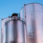 Zwei große metallische Hochdruck-Wärmespeicher-Silos ragen in Simmering vor einem strahlend blauen Himmel empor.