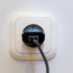 Eine weiße Wandsteckdose mit eingestecktem schwarzen Stecker.