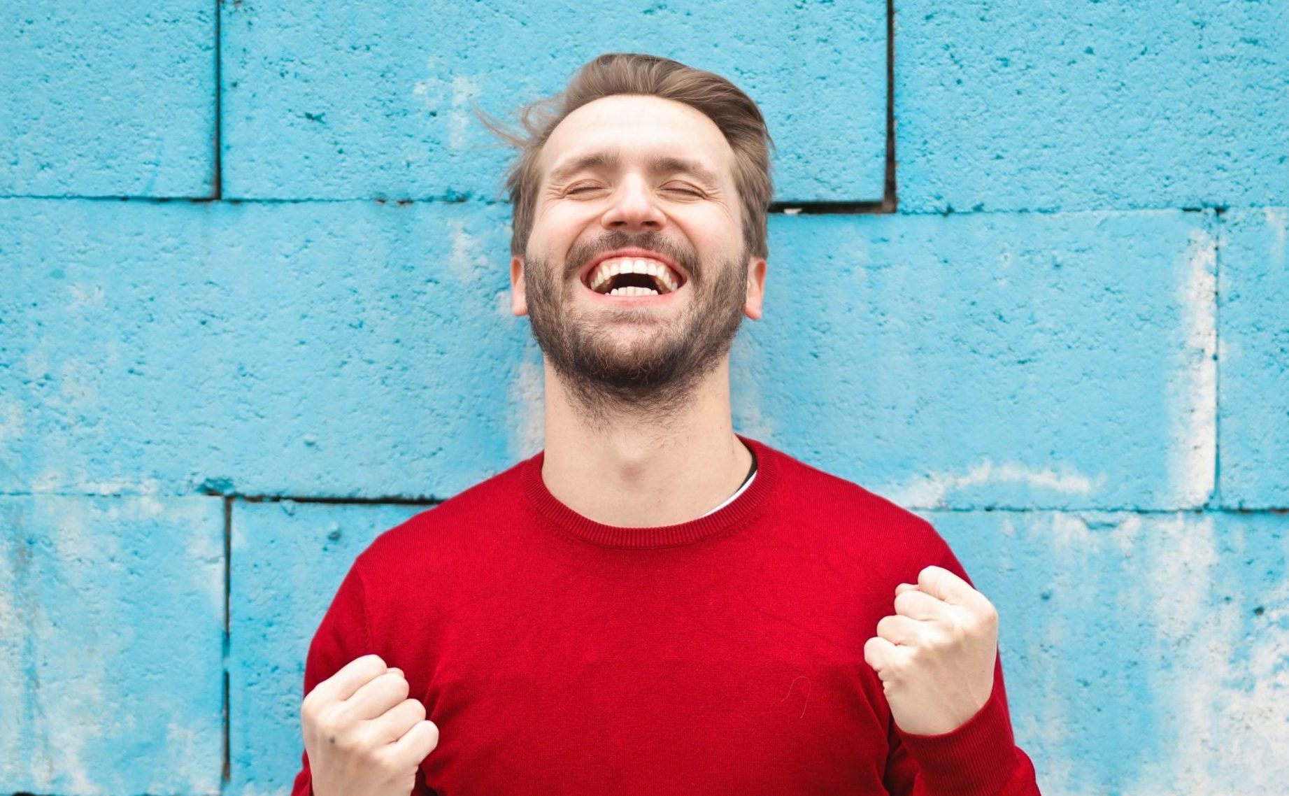 Mann steht vor blauer Wand und jubelt