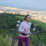 Eine Frau joggt auf einem Hügel mit der Wiener Stadtlandschaft im Hintergrund.