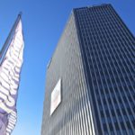 Hoher, dunkelgrauer Wolkenkratzer der Firmenzentrale Wien Energie in Erdberg unter den klaren blauen Himmel, im Vordergrund weht eine Flagge "TownTown" an einem Mast.