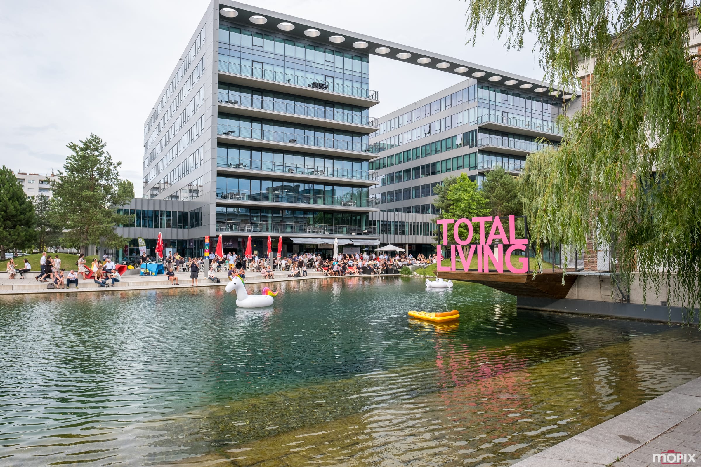 Moderne Bürogebäude "Viertel Zwei" am Wasser, Menschen, die auf der Wiese sitzen, und im Wasser spielen.