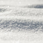 Nahaufnahme einer glitzernden, schneebedeckten Oberfläche mit sanften Wellen und subtilen Schatten.