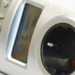 Silberner digitaler Timer-Stecker mit LCD-Display und drei Tasten mit den Beschriftungen „Modus“, „Auf“, „Ab“ und „OK“.