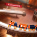 Spielzeugeisenbahn auf einem Holztisch mit einer Strecke, die sich um kleine Gebäude windet.