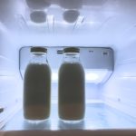 Zwei Milchflaschen mit Deckel in einem offenen, von hinten beleuchteten Kühlschrank.