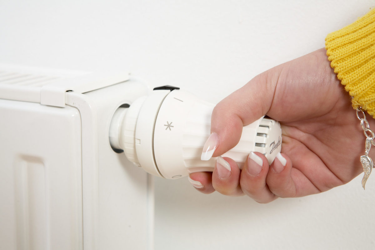 Frauenhand dreht an Heizkörperthermostat