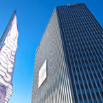 Hohes, modernes Bürogebäude, die Wien Energie Zentrale, vor einem klaren, blauen Himmel mit der "TownTown"-Flagge im Vordergrund.