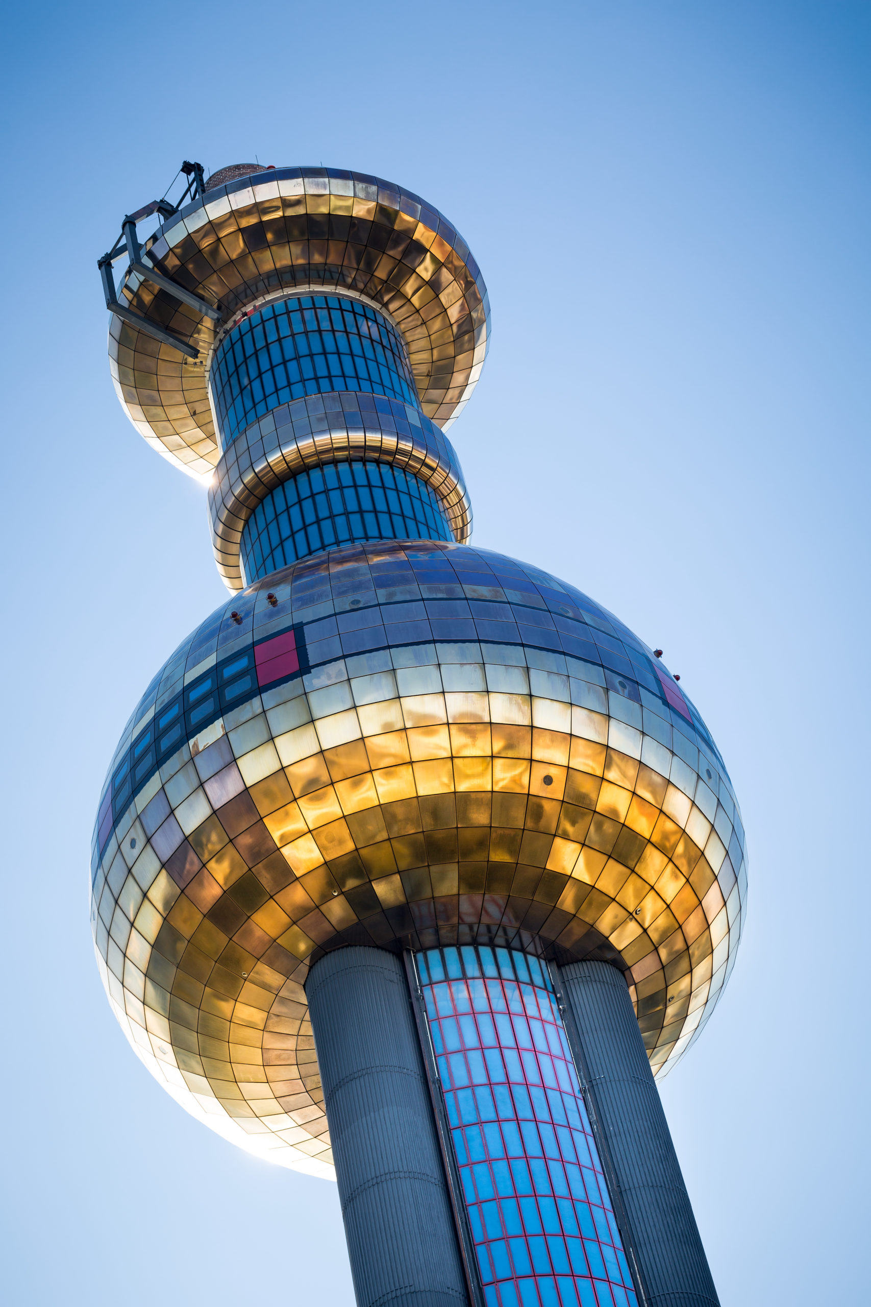 Der moderne Turm der Spittelau mit der goldenen, reflektierenden Kugel vor einem klaren blauen Himmel.
