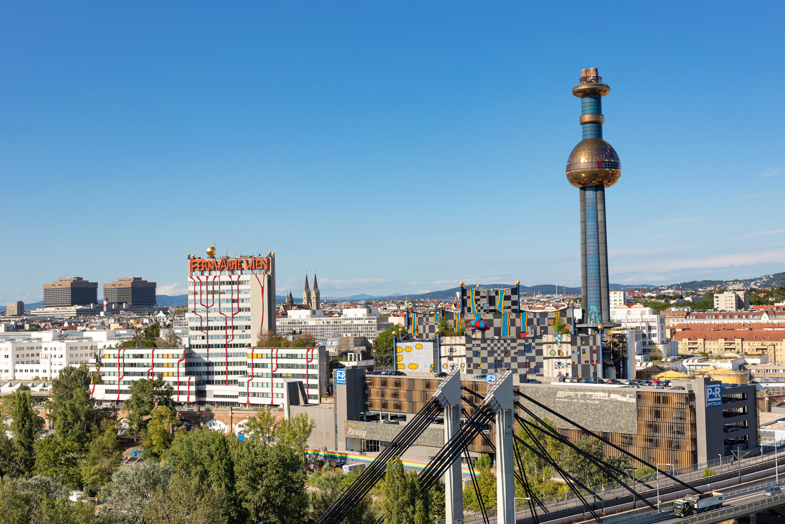 Wiener Stadtlandschaft mit modernen Gebäuden, darunter der markante Turm der Spittelau mit der goldenen Kugel unter einem klaren blauen Himmel.