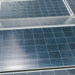 Nahaufnahme mehrerer gitterförmig angeordneter Solarmodule, die das Sonnenlicht reflektieren.