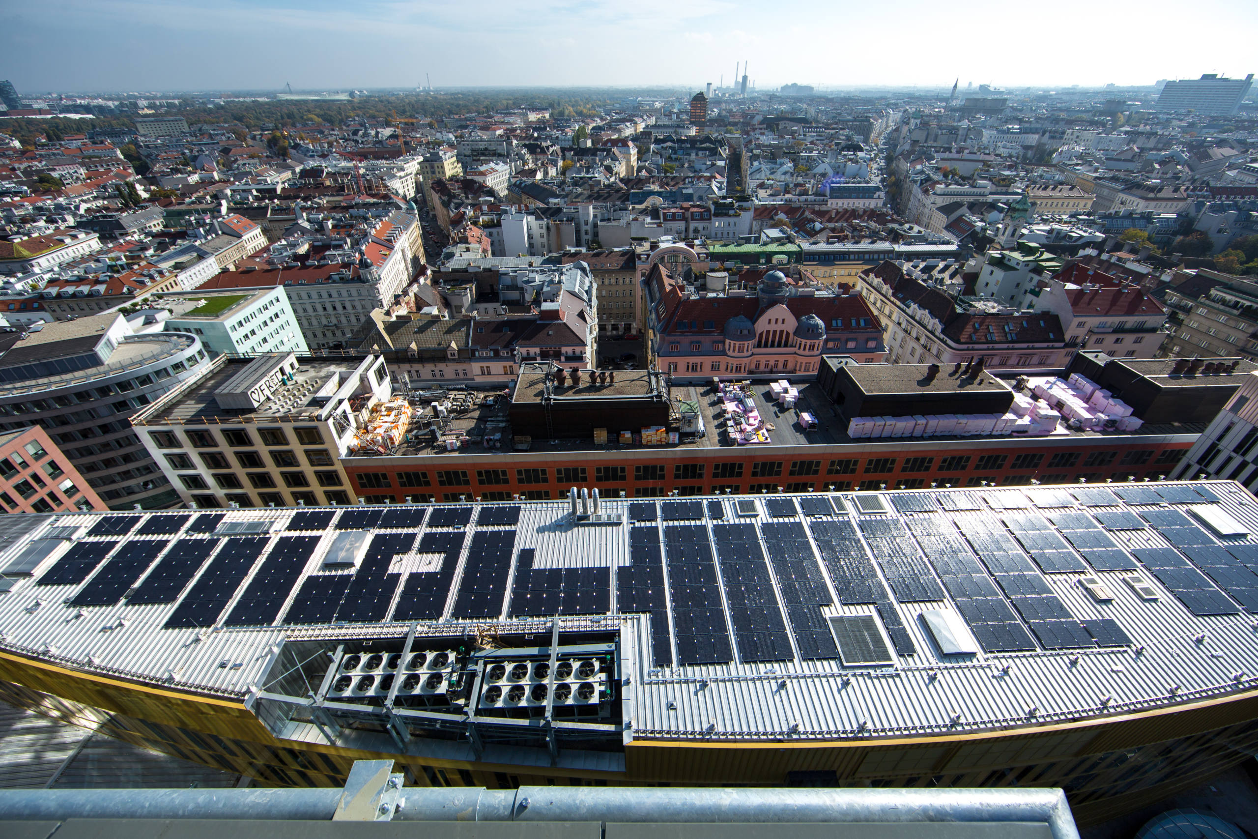 Luftaufnahme einer Stadtlandschaft mit Gebäuden und Dächern an einem sonnigen Tag. Im Fokus das Einkaufszentrum "The Mall" in Wien-Landstraße, wo 1.400 PV-Module verbaut wurden.