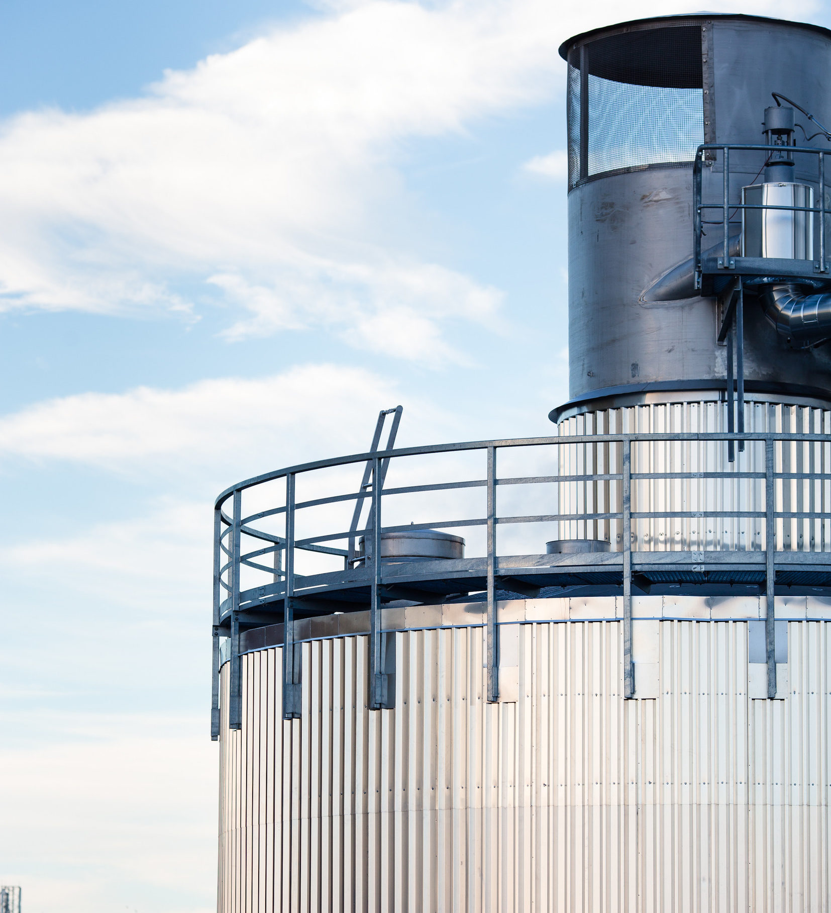Großwärmespeicher in zylindrischer Form vor einem blauen Himmel mit vereinzelten Wolken.