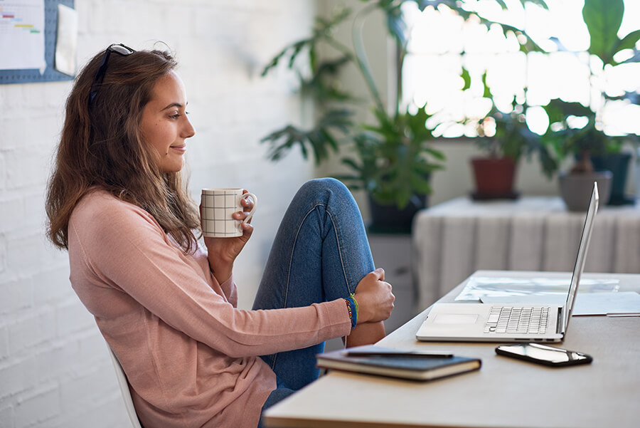 Eine Frau sitzt mit einem Becher Kaffee vor einem Laptop