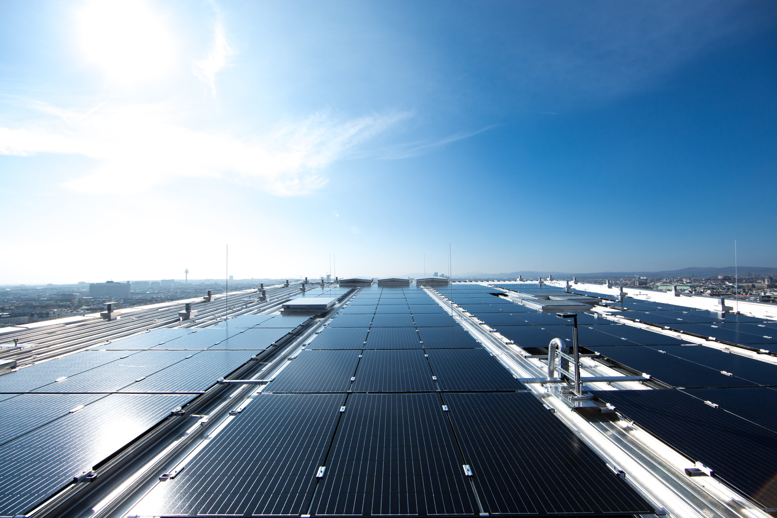 Weitwinkelansicht von Solarmodulen auf dem Dach des neuen Bahnhofs "Wien Mitte". Klarer, blauer Himmel, die Sonne scheint hell.