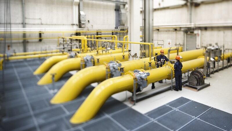 Zwei Arbeiter inspizieren den Erdgasdispatcher in Simmering. Im Raum sind große gelbe Rohre.