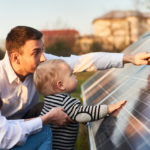 Eine Familie mit einem kleinen Kind betrachtet und berührt eine Photovoltaikanlage im Freien an einem sonnigen Tag.