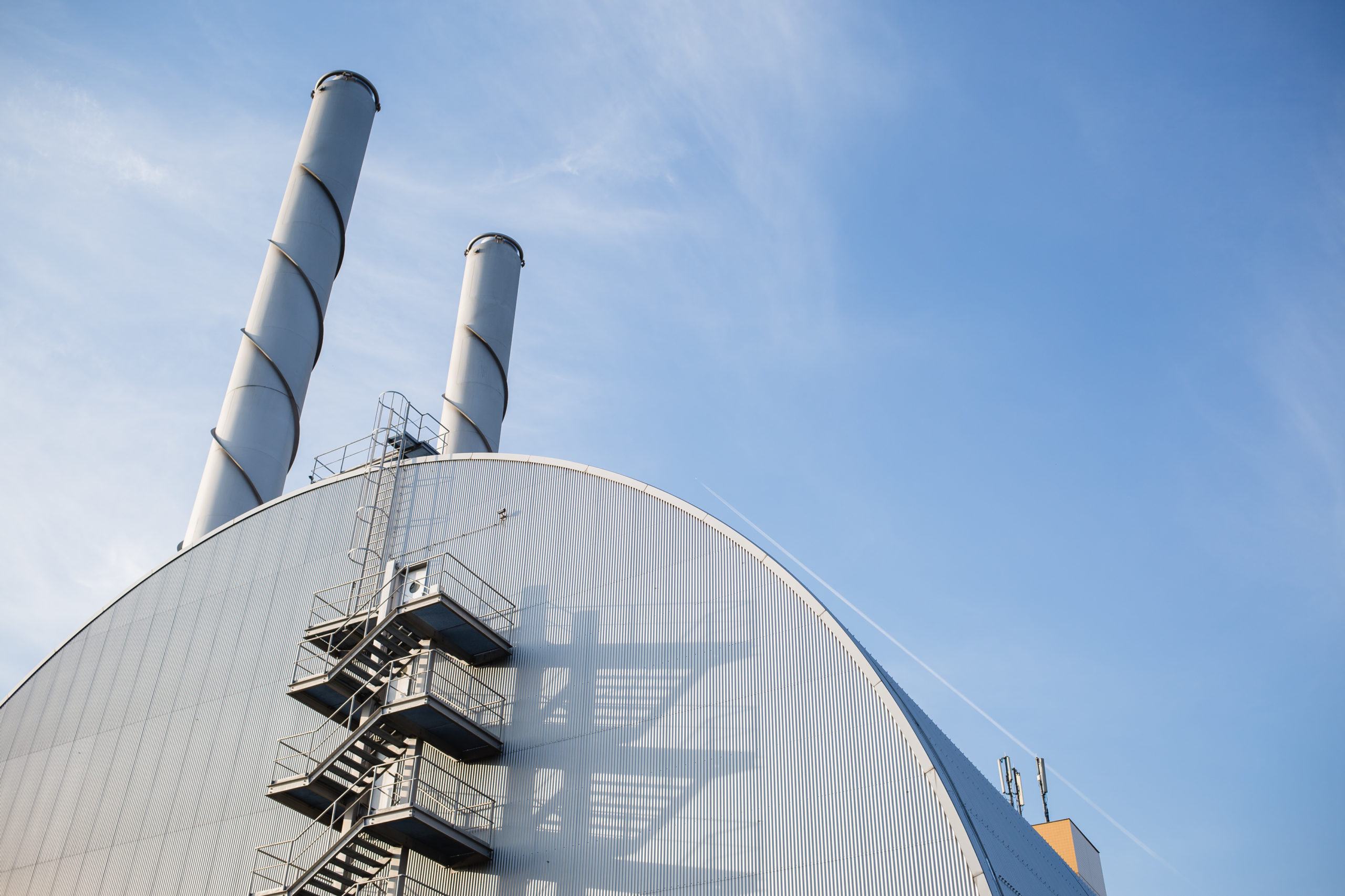 Fernheizwerk Inzersdorf Süd mit zwei Schornsteinen vor einem klaren blauen Himmel.