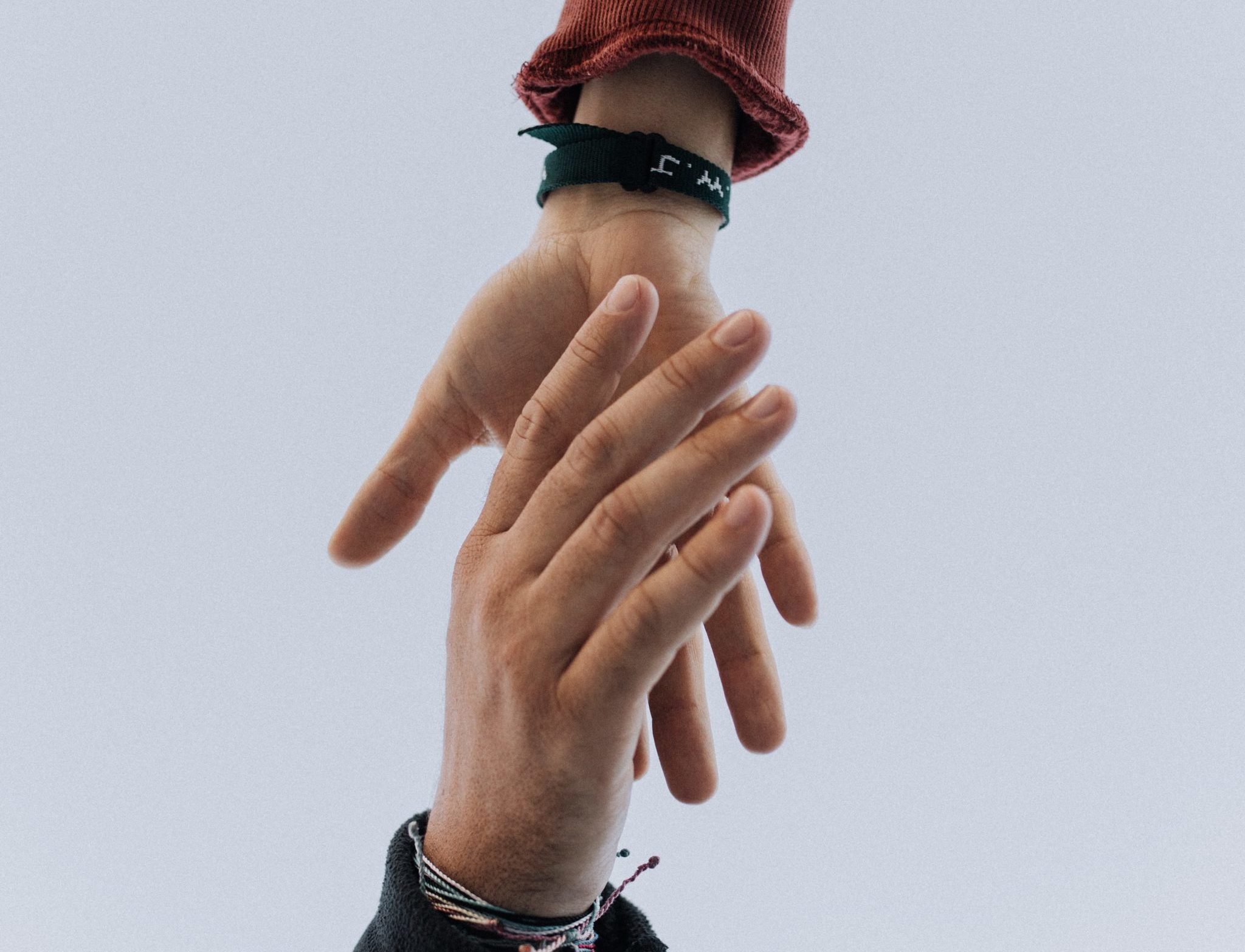 Zwei Hände, die sich vor einem grauen Himmel nacheinander ausstrecken, eine trägt ein Armband.