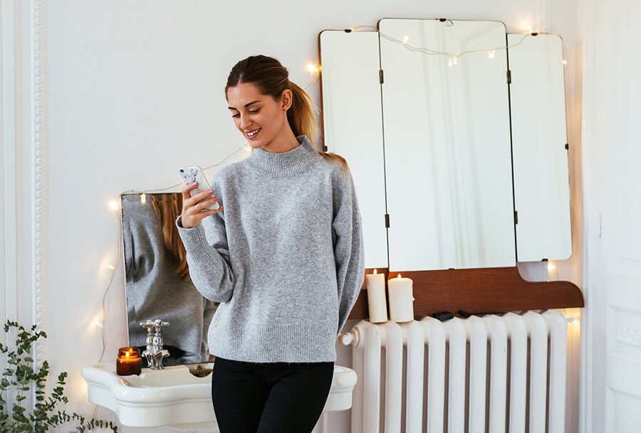 Eine Frau lehnt an einem Heizkörper und schaut auf ihr Smartphone