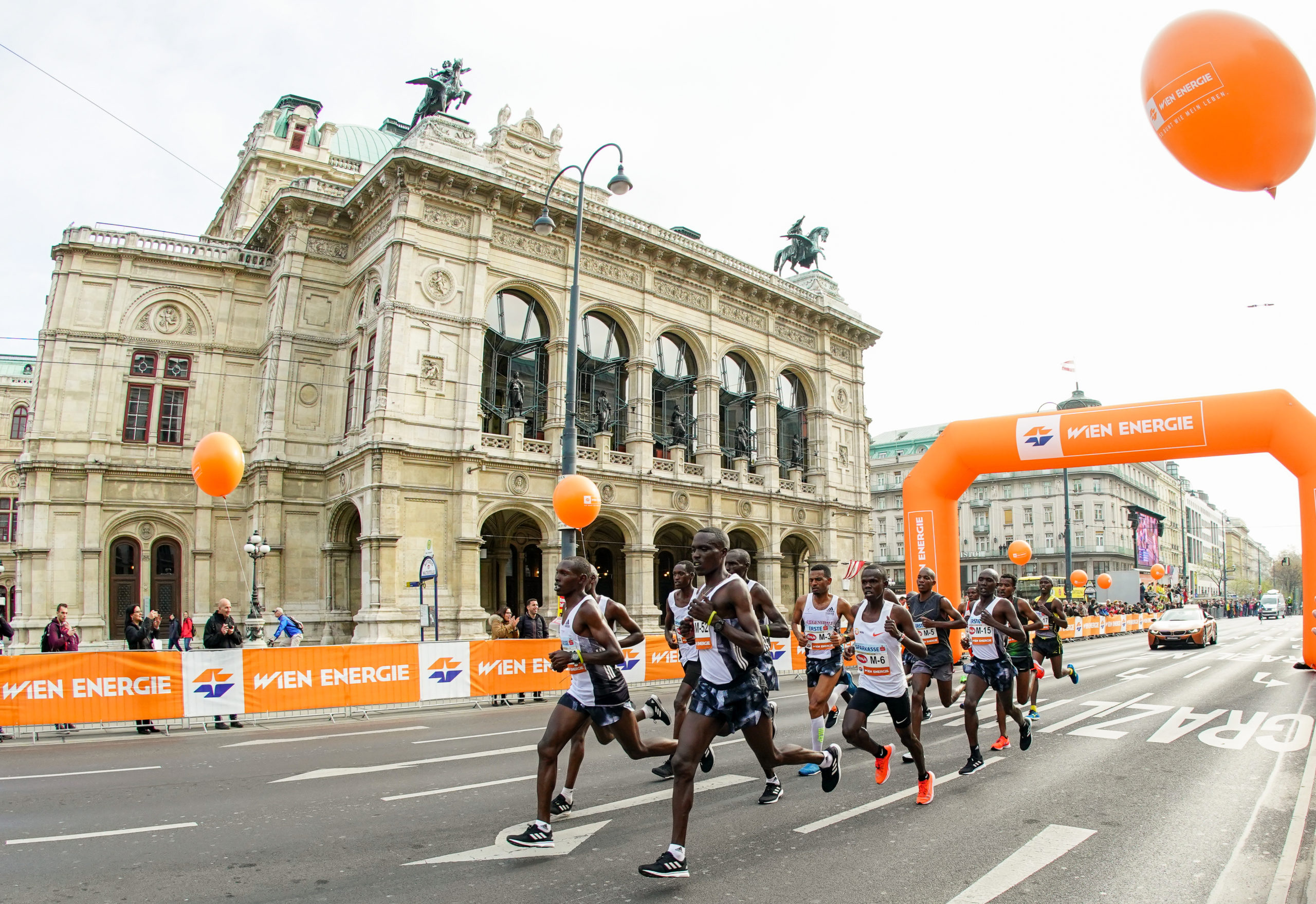 Die Läufer treten beim Vienna City Marathon in der Nähe der Oper an. Orangefarbene Luftballons und Banner verleihen der lebhaften Veranstaltung eine festliche Note.