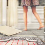 Bodenaufbau bei Fußbodenkühlung. Rohre sind vom Estrich umgeben, darauf befindet sich der Fliesenkleber und der Bodenbelag.