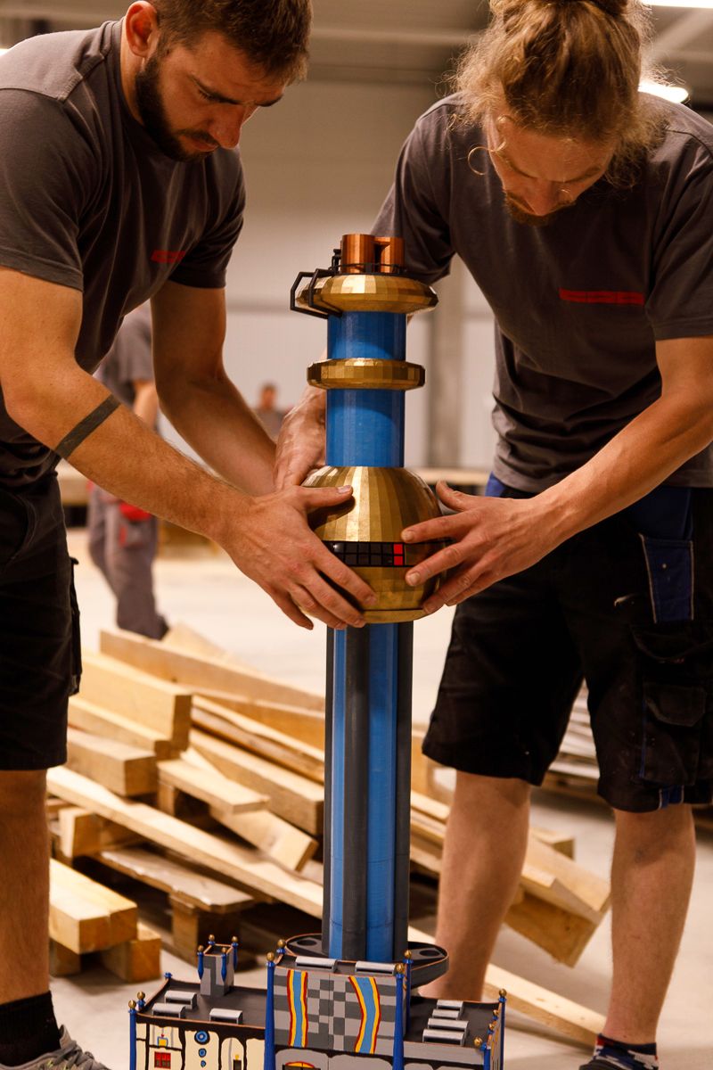 Zwei Männer bauen im Innenbereich ein Modell der Spittelau auf. Im Hintergrund sind Holzbretter zu sehen.