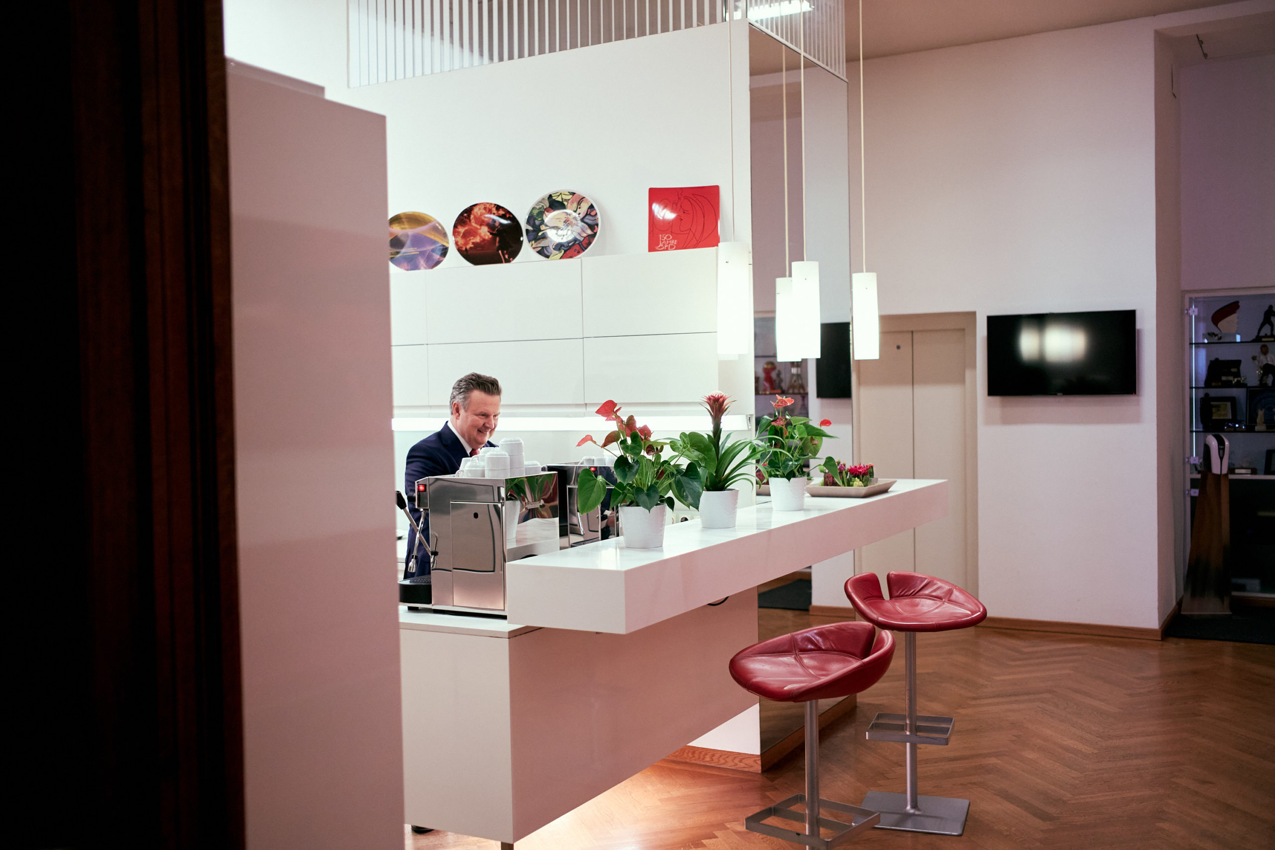 Michael Ludwig an einer modernen Café-Theke mit Pflanzen, roten Stühlen und Wanddekor in einem gemütlichen Innenambiente.