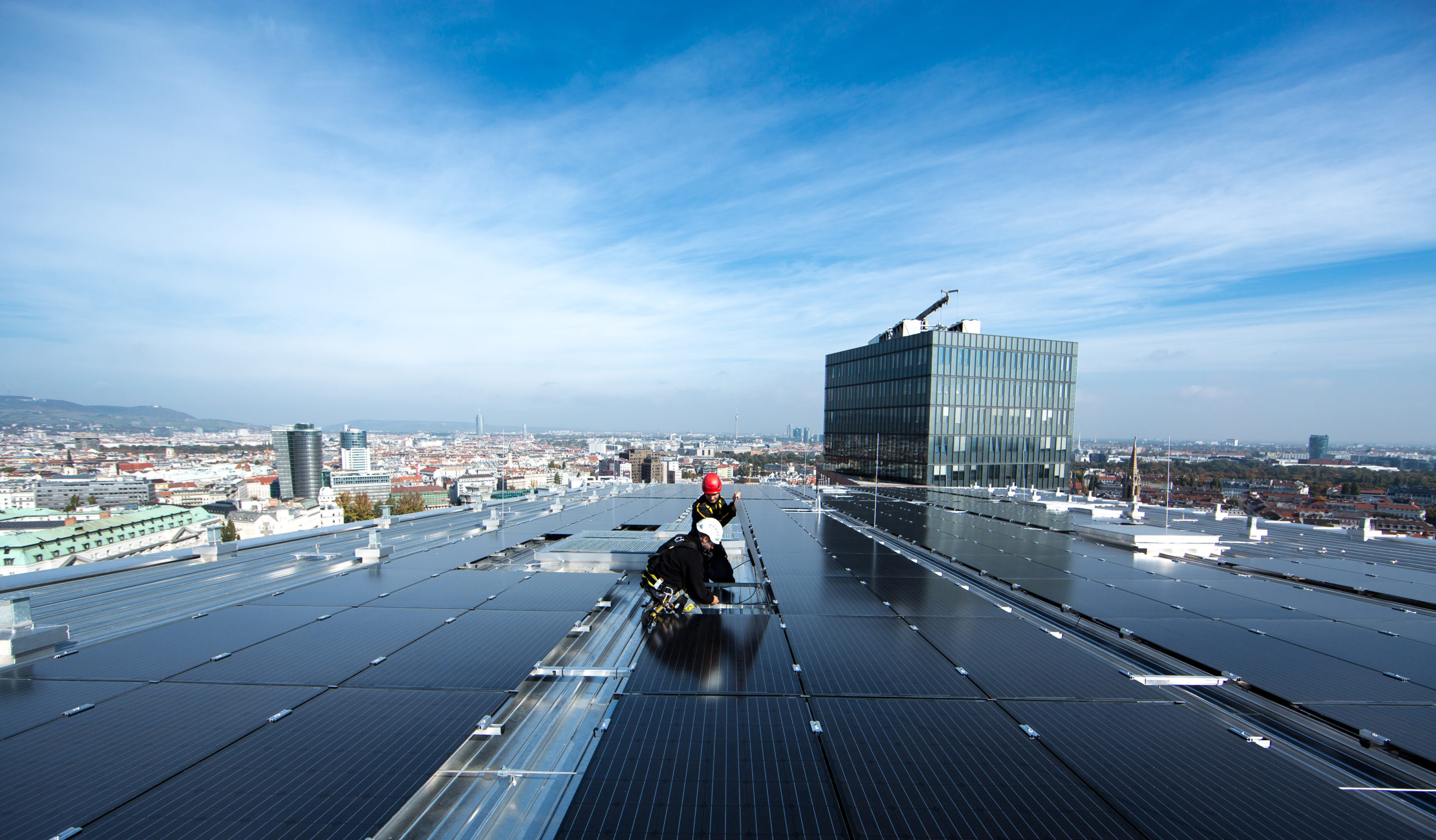 Arbeiter installieren Solarmodule auf dem Haus des Meeeres mit Blick auf Wien unter einem klaren blauen Himmel.