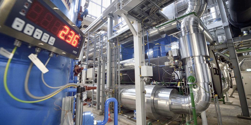 Großwärmepumpe mit großen Rohren und einer Digitalanzeige mit der Zahl 236. Hell erleuchtete Fabrikumgebung.