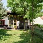 Begrüntes Dach des Kunsthauses in Wien, mit Garten und Bäumen. Im Hintergrund ist eine kleine Stadtwohnung zu erkennen.