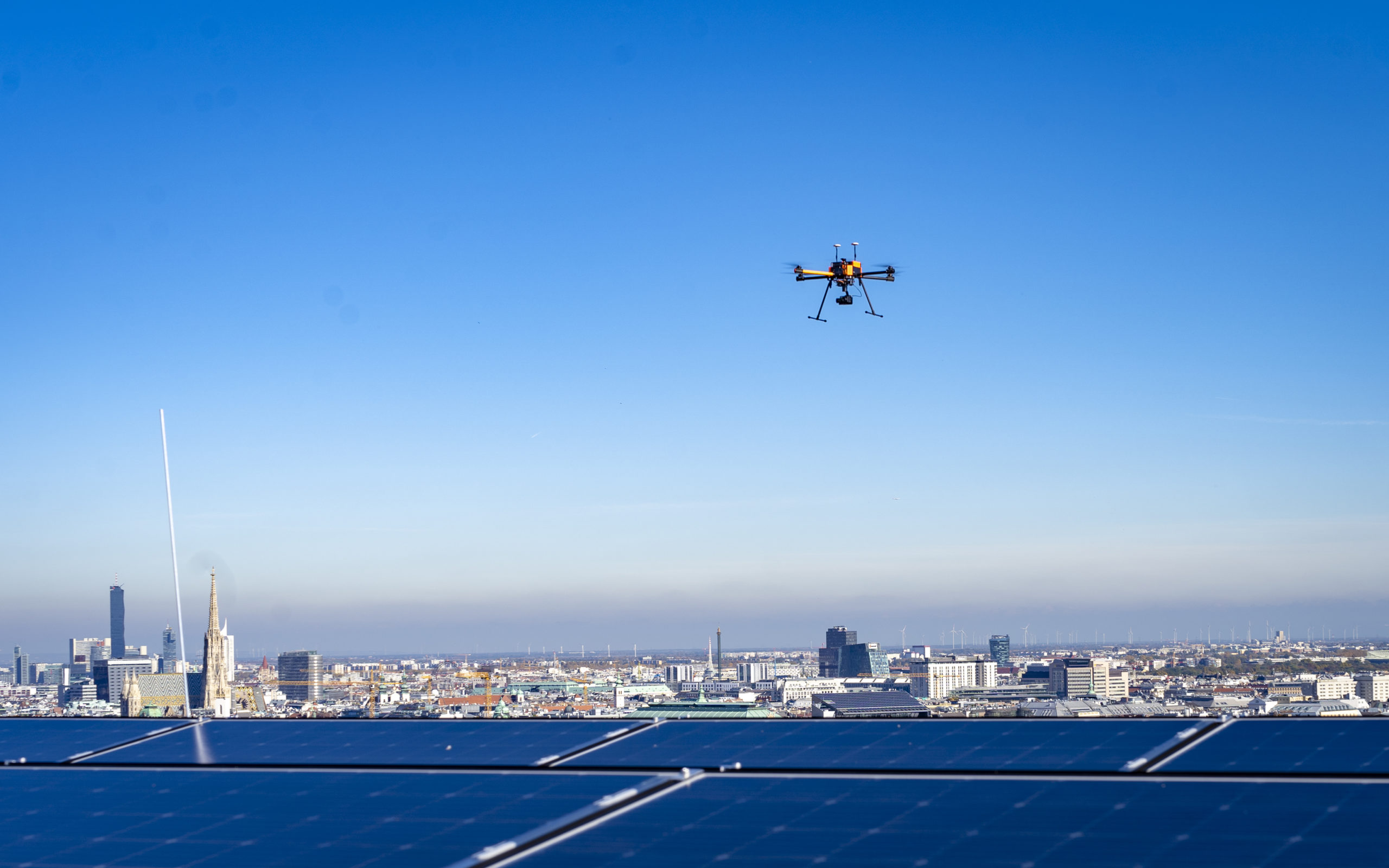 Drohne fliegt über die Solarmodule des Haus des Meeres. Im Hintergrund ist das Wiener Stadtbild bei klarem, blauen Himmel zu sehen.