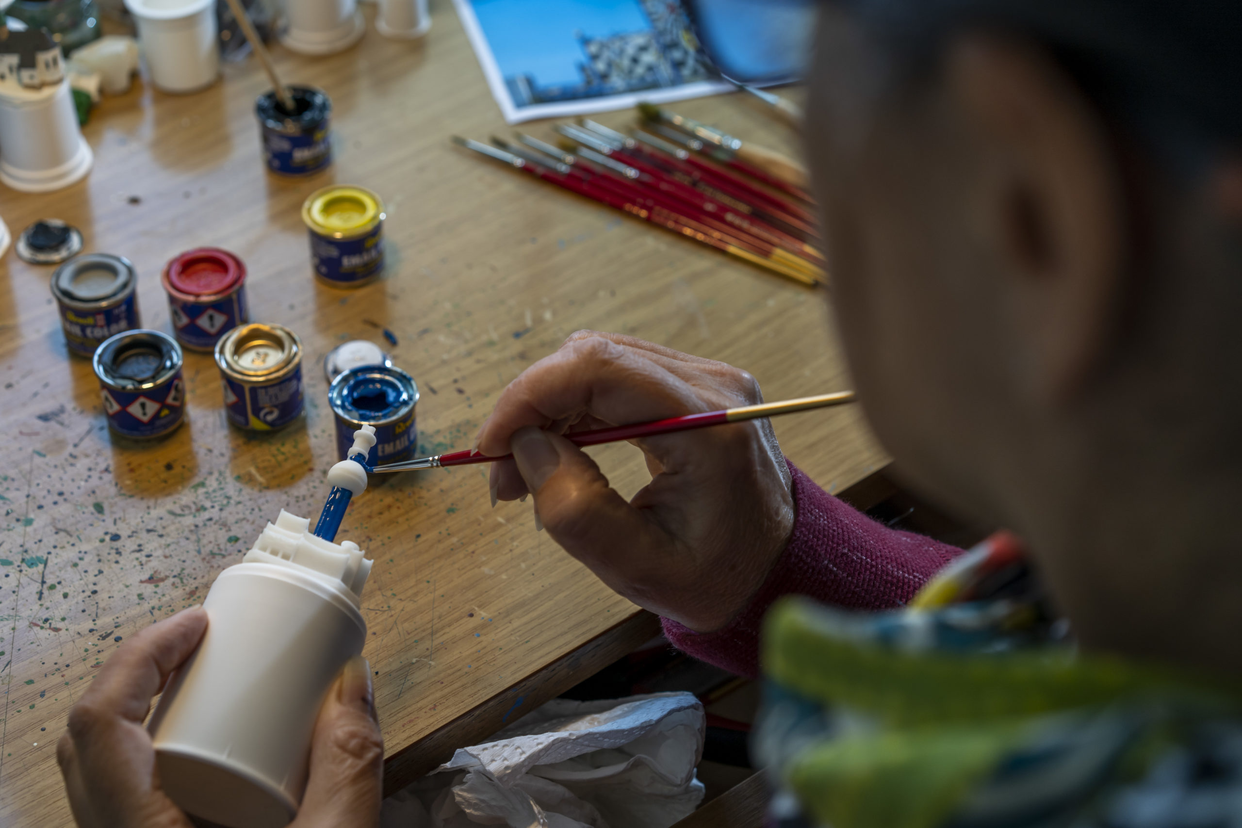 Person bemalt ein weißes Spittelau Modell mit blauer Farbe an einem Arbeitstisch.