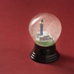 Eine Schneekugel mit der Spittelau im Inneren vor einem schlichten roten Hintergrund.