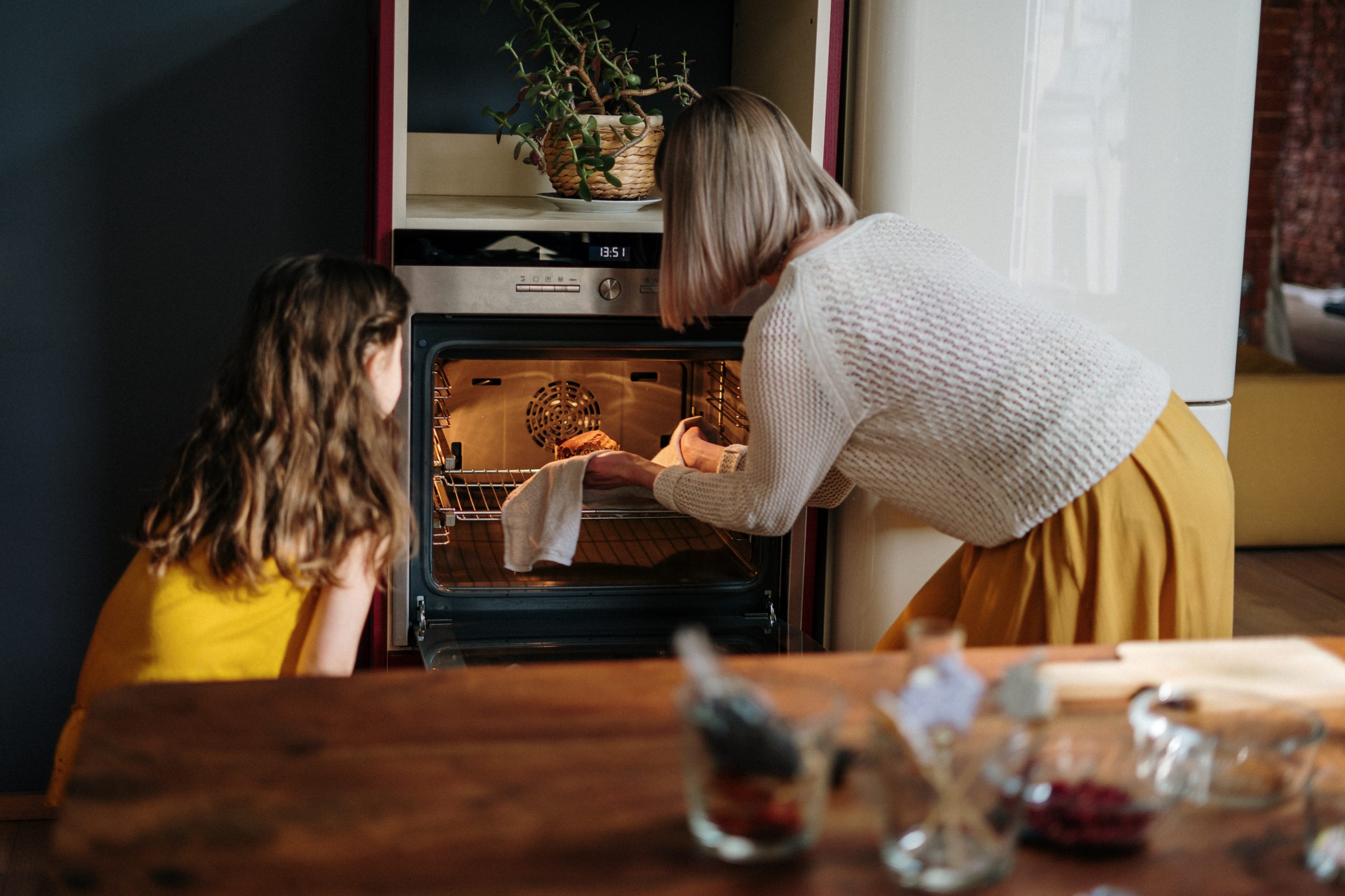 Frau und Kind stehen vor einem Backofen und holen einen Kuchen heraus.