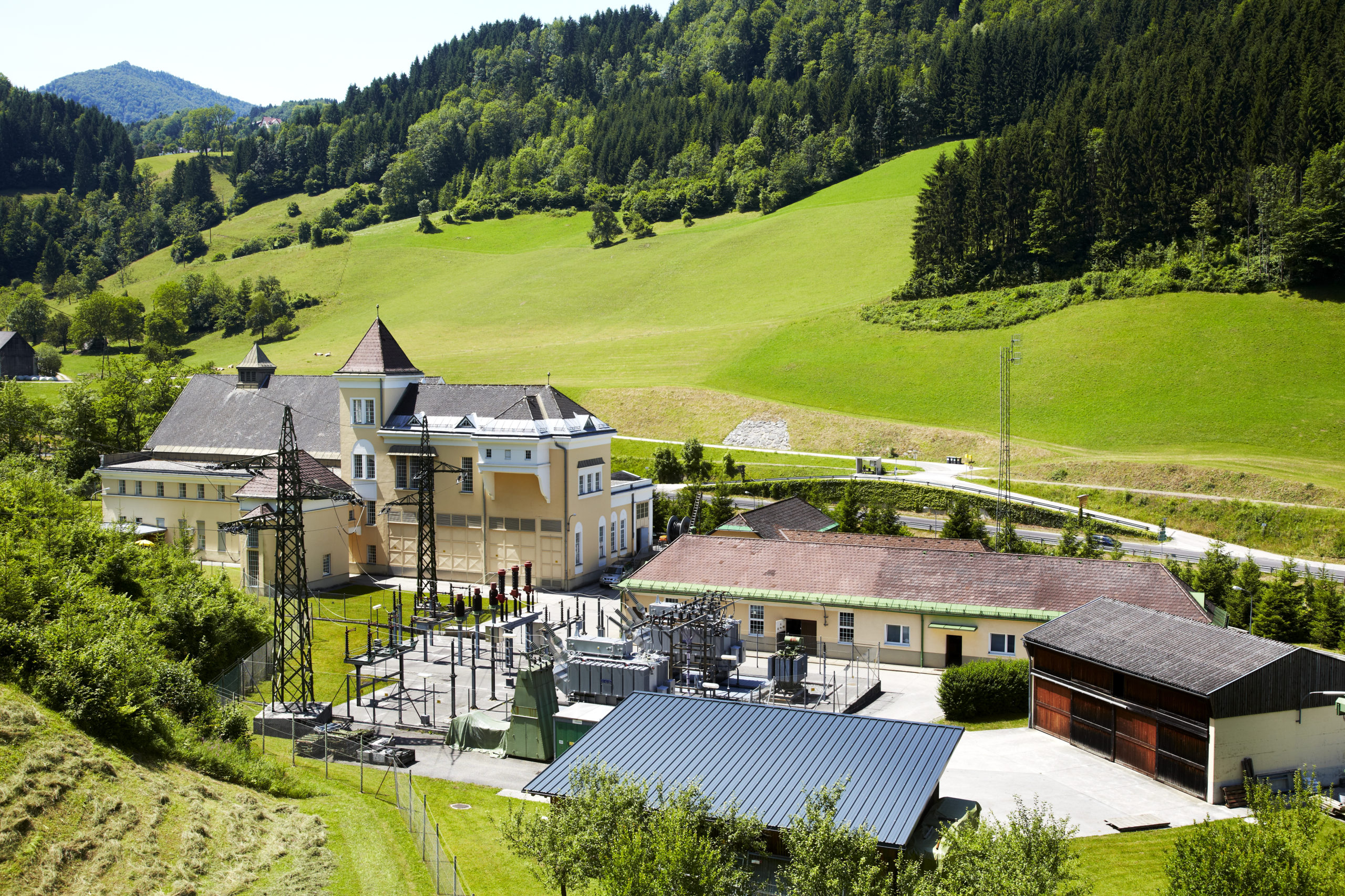 Eingebettet in ein üppig grünes Tal sind das gelbe Gebäude des Wasserkraftwerks Opponitz von Bäumen und sanften Hügeln umgeben.