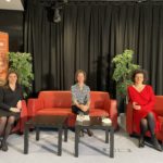 Drei Frauen sitzen auf roten Stühlen vor einem schwarzen Vorhang, neben ihnen hängt ein „WIEN ENERGIE“-Banner. Claudia Novak ist bei dieser Women on Stage-Veranstaltung am 8. März 2021 gemeinsam mit ihren Mitrednerinnen Gundi Mayrhofer und Theresa Teufel dabei.