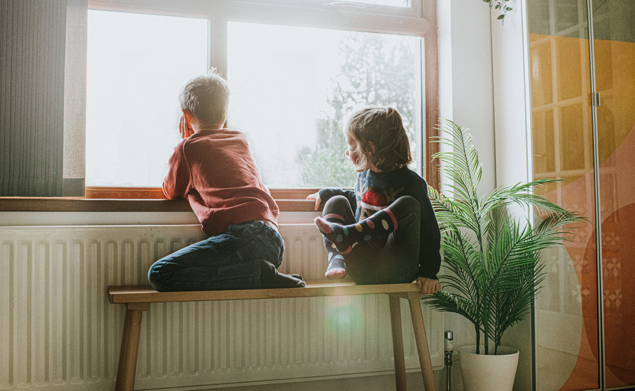 Young Girl and Boy sit on a Bench by a Sunny Window and Gaze out
