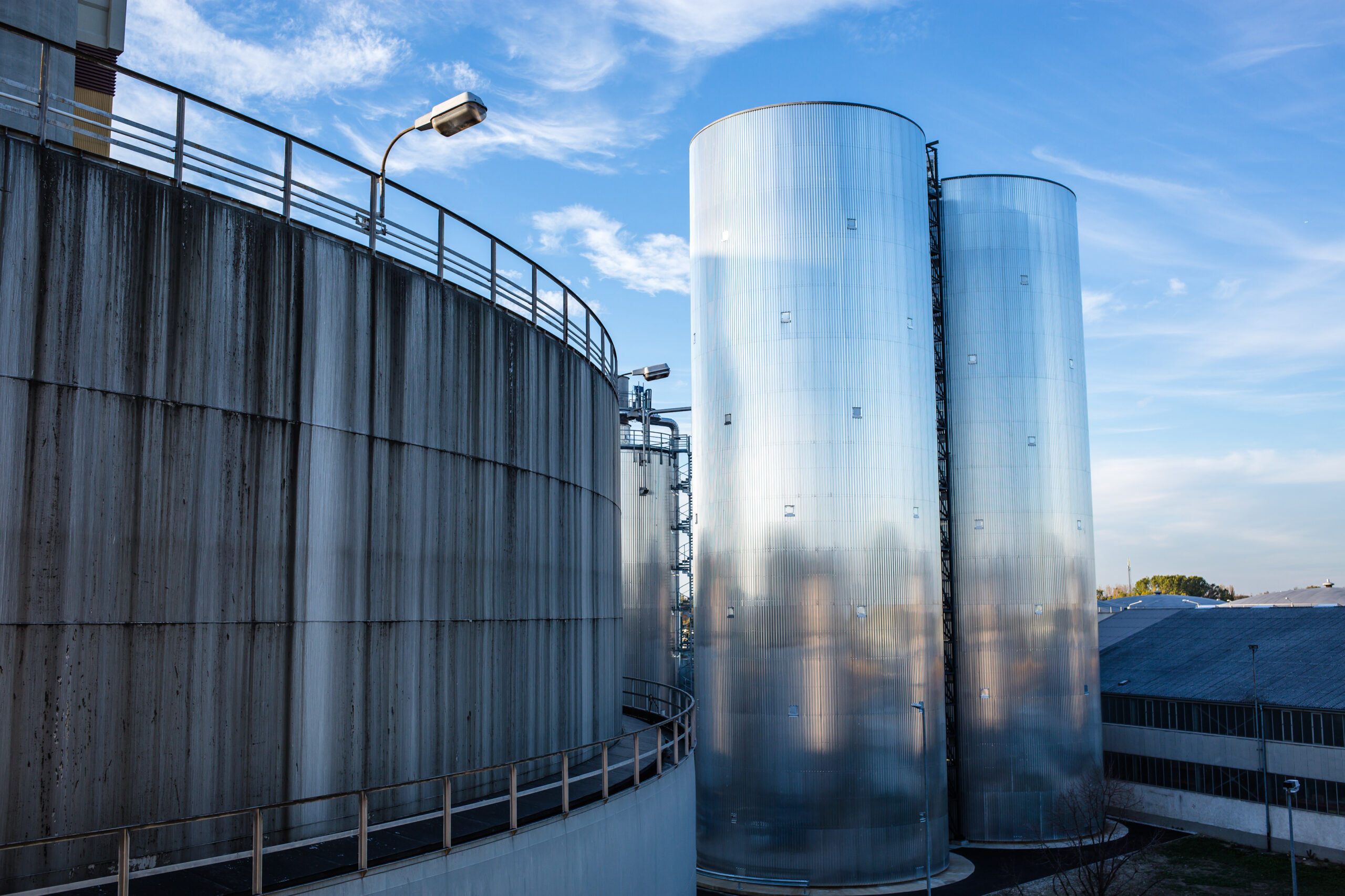 Zwei große Wärmespeicher, in denen sich der Himmel spiegelt, mit einer Betonkonstruktion auf der linken Seite unter einem Laternenpfahl.