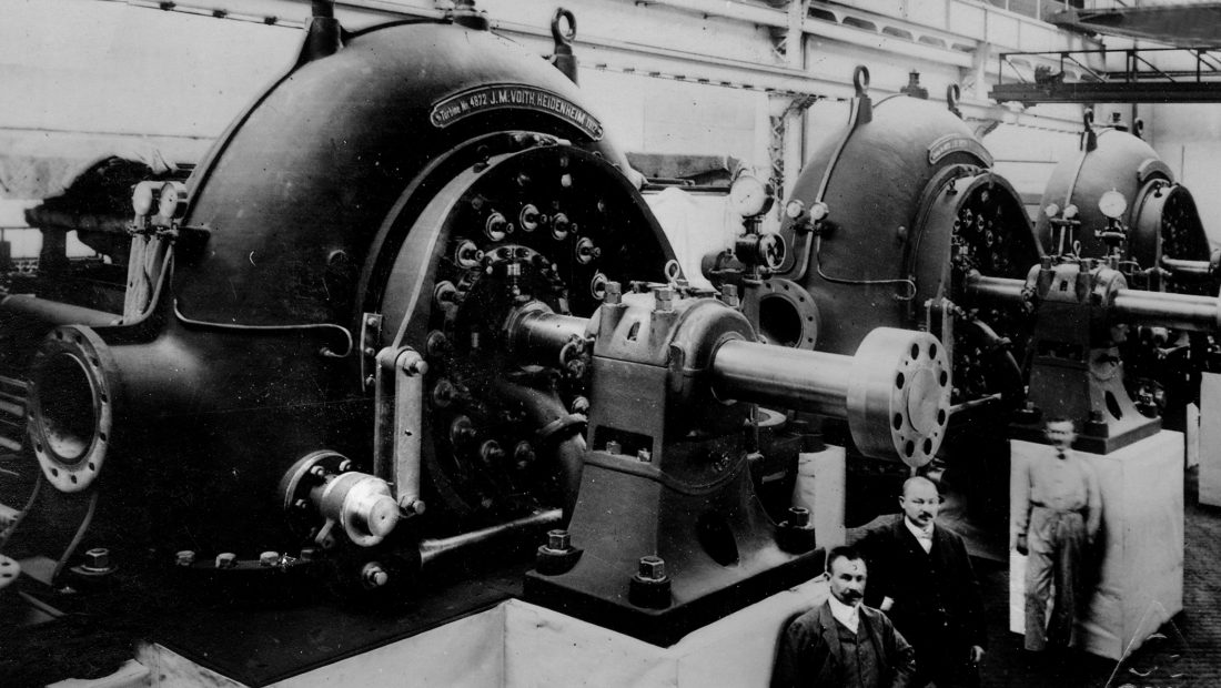 Schwarzweißfoto von Männern, die im Wasserkraftwerk Opponitz vor einem großen Drehkolben stehen.